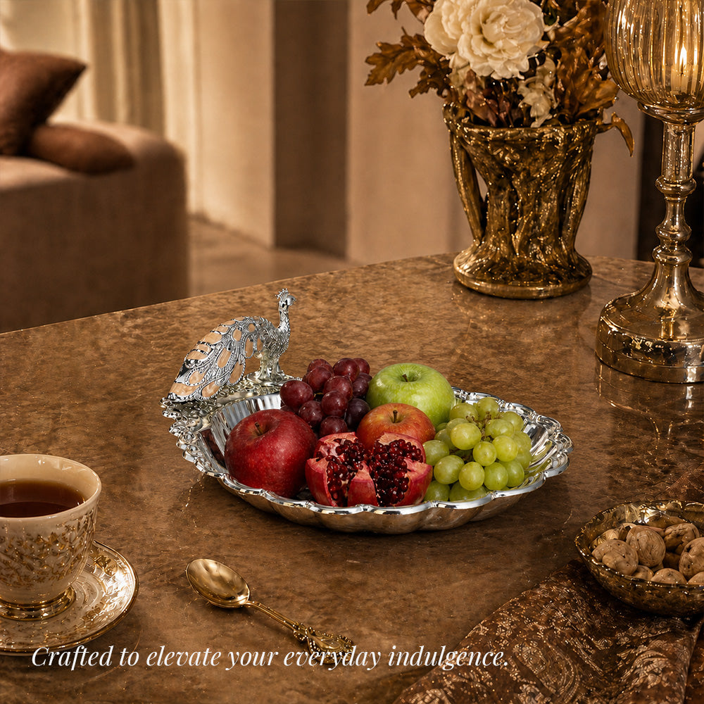 Diviniti Amber Peacock German Silver Dry Fruit Bowl on a table with assorted fruits and elegant decor.