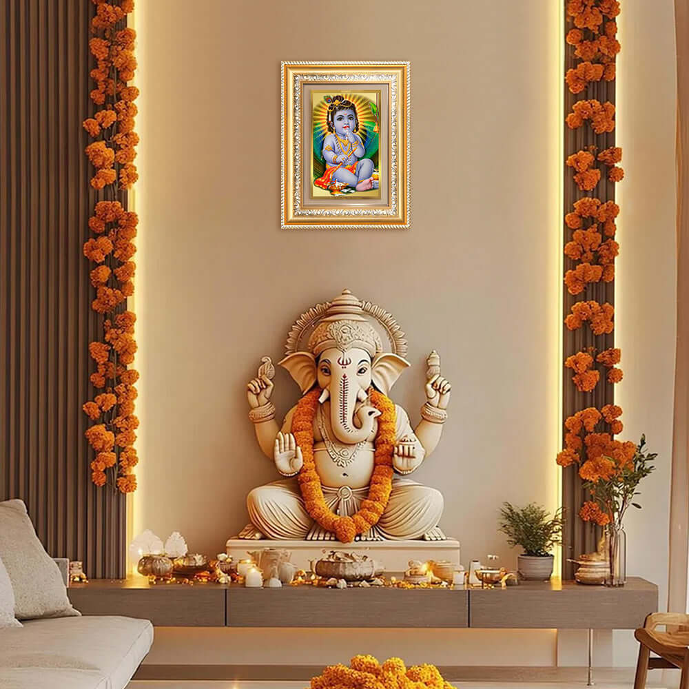 Devakinandana Wall and Tabletop Photo Frame showcasing Bal Gopal above an ornate Ganesh statue, adorned with marigold garlands.