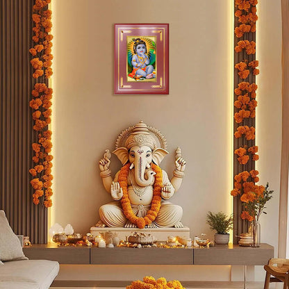 Baby Krishna photo frame displayed above a serene Ganesha idol in a decorated indoor setting.