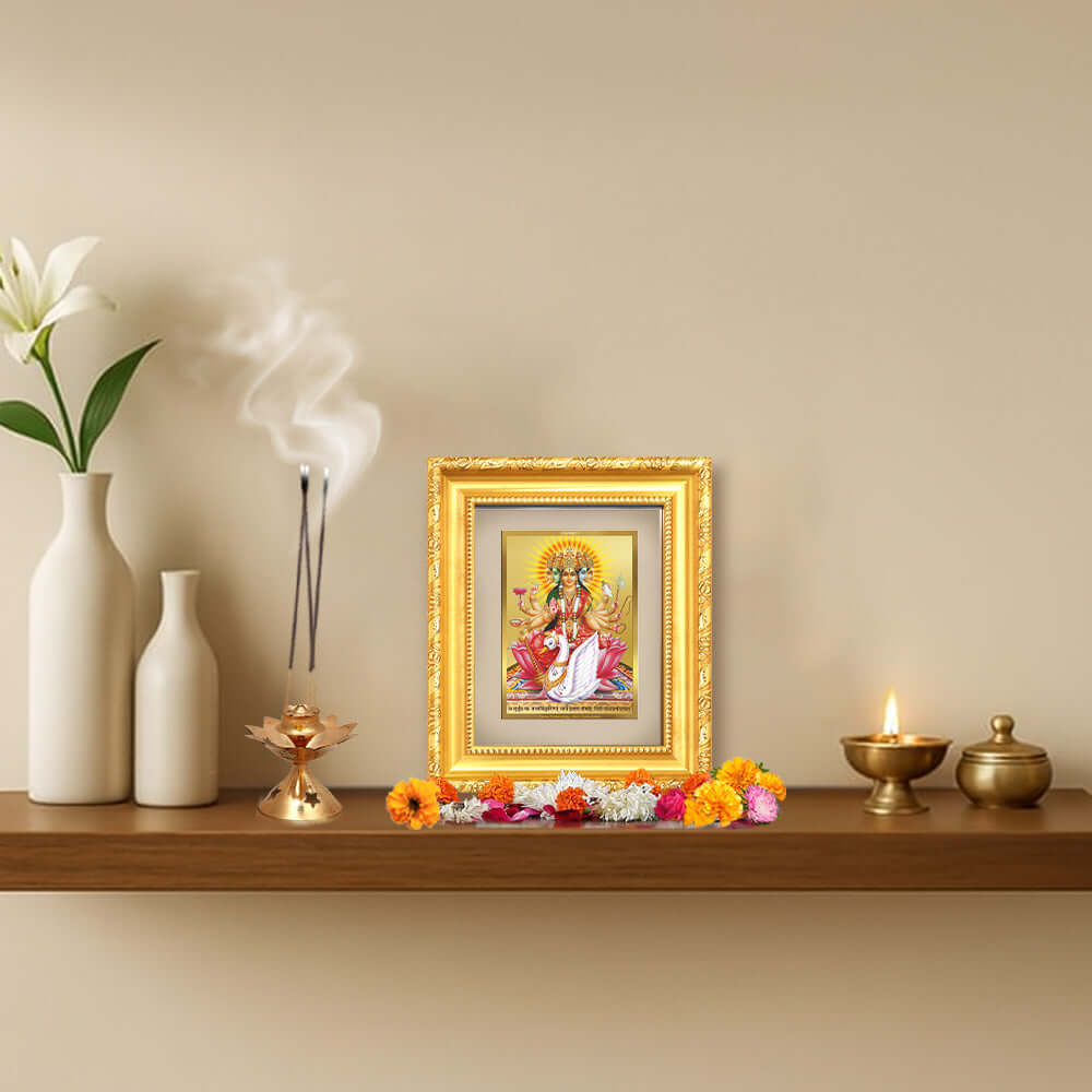 Gayatri Mata tabletop frame in 24K gold plated foil displayed on a shelf with decorative elements.