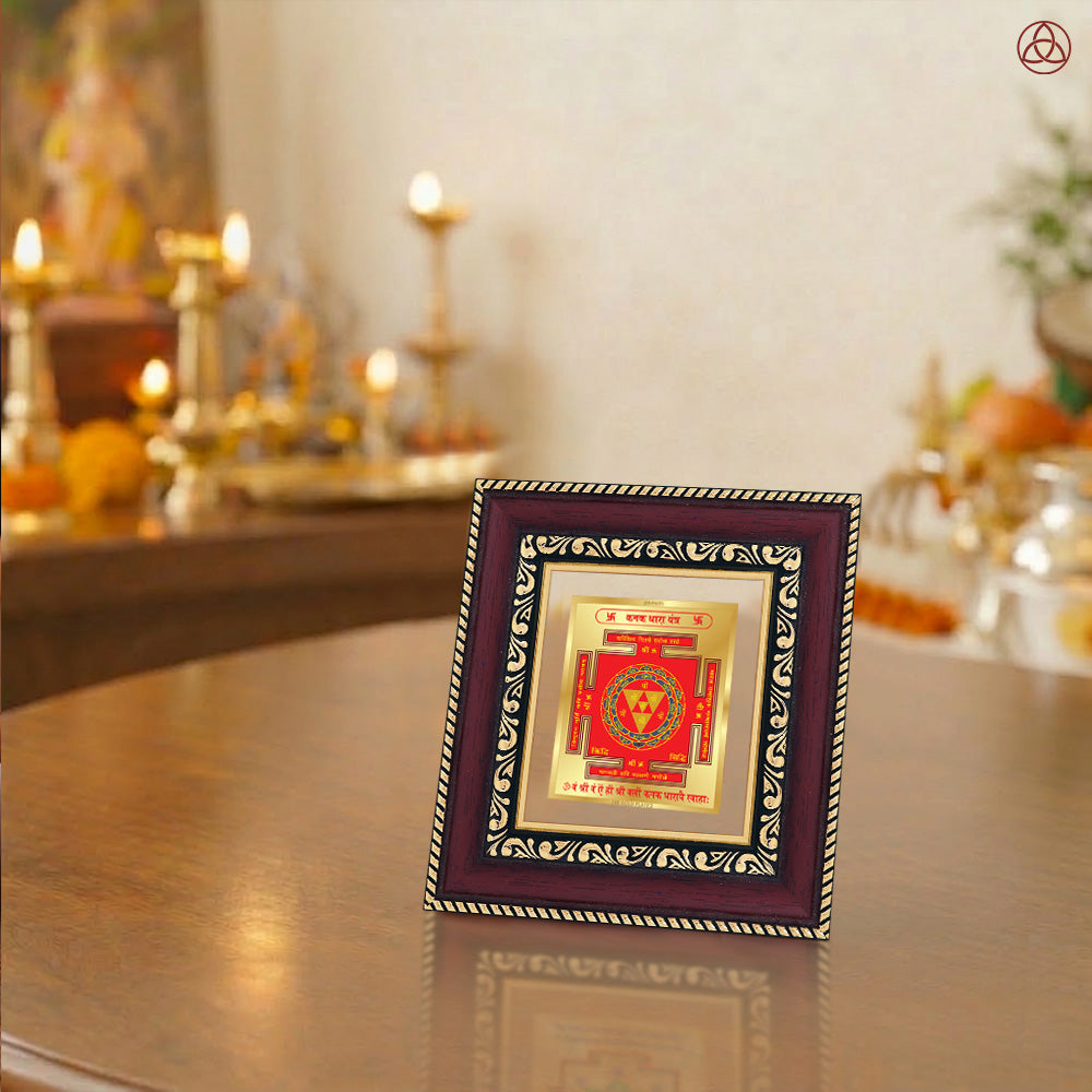 Kanak Dhara Yantra framed on a wooden table with a decorative background featuring warm lighting and spiritual elements.