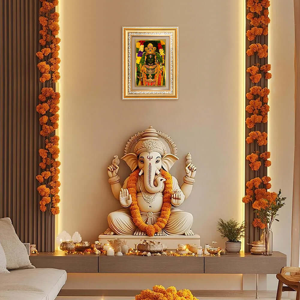Elegant Ganesh statue adorned with garlands and a colorful framed photo on the wall in a beautiful home decor setting.