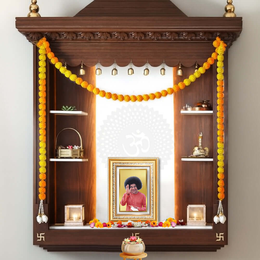 Sathya Sai Baba wall photo frame adorned with marigold garlands in a decorated wooden altar.