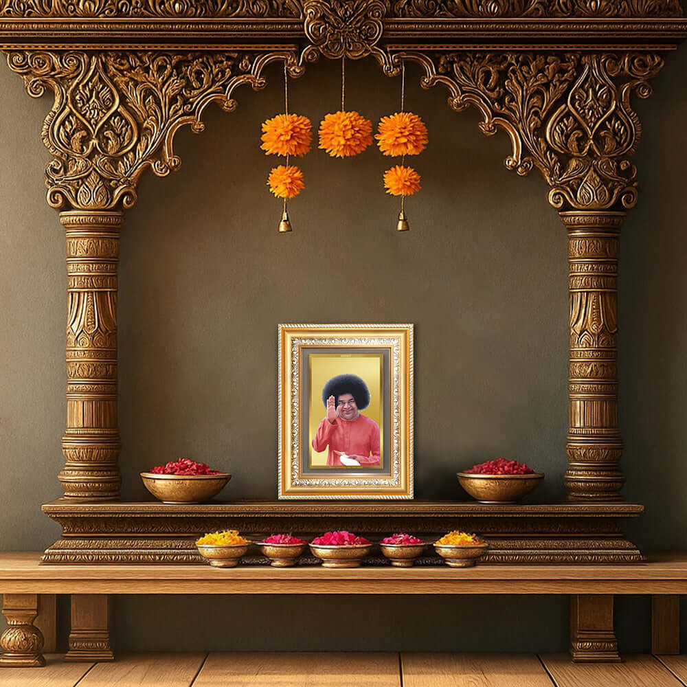 Sathya Sai Baba framed photo in gold frame on ornate wooden altar with flowers and bowls.